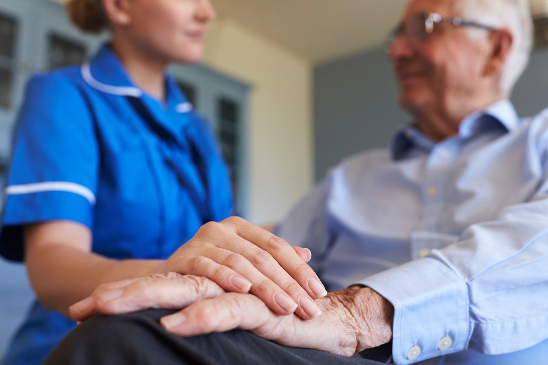 Nurse Talking With Senior Man Sitting In Chair On Home Visit